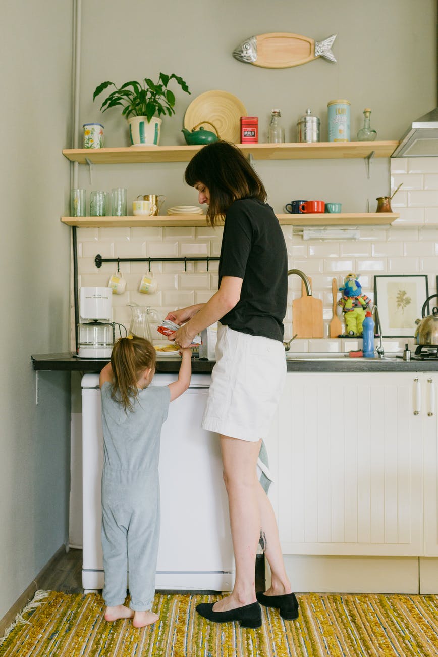 young mother with little daughter preparing breakfast in kitchen