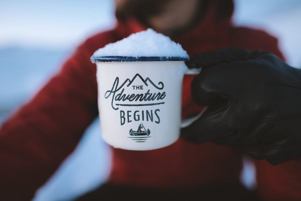 selective focus photography of person holding the adventure begins mug