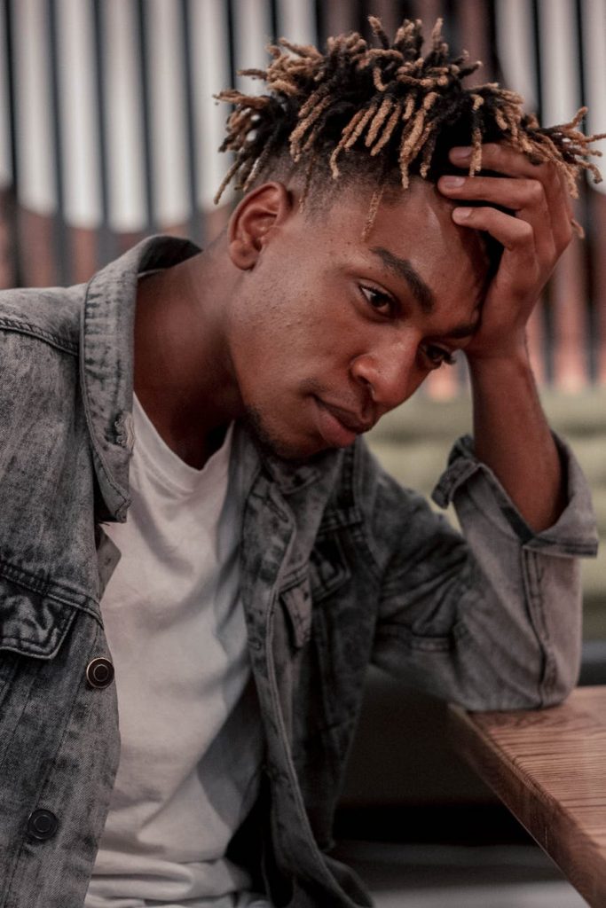 pensive black man with dreadlocks leaning on hand