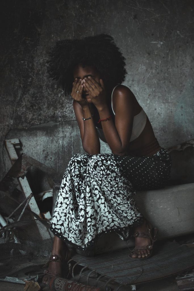 tired black woman covering face while sitting in messy room