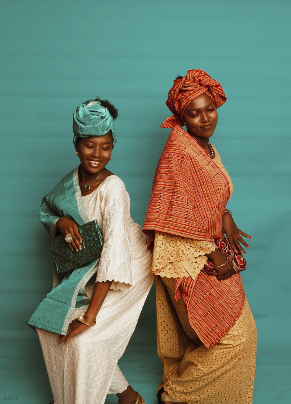 black women in traditional dresses and headdress near blue wall